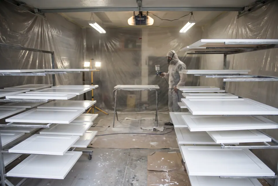 Cabinet doors sprayed with white enamel drying on racks in a work area.