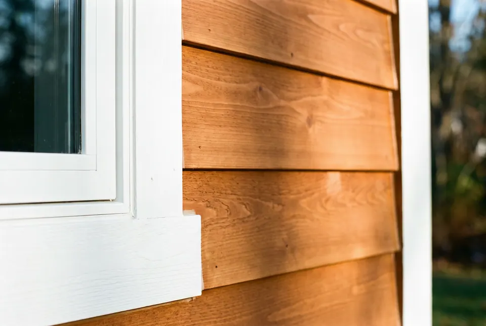 Close-up of stained cedar lap siding meeting crisp white painted trim at a window corner