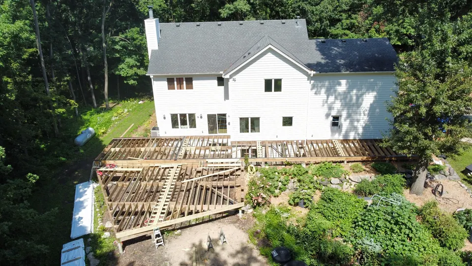 Aerial view of a white two-story home with an asphalt shingle roof and new deck framing below it