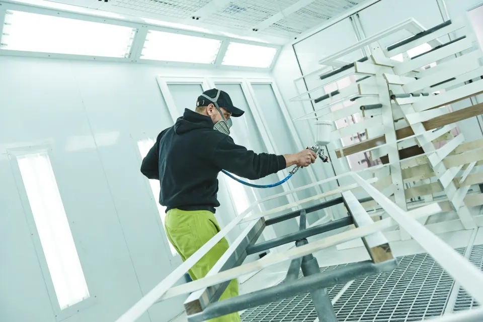 A painter spraying white enamel on trim pieces in a spray booth